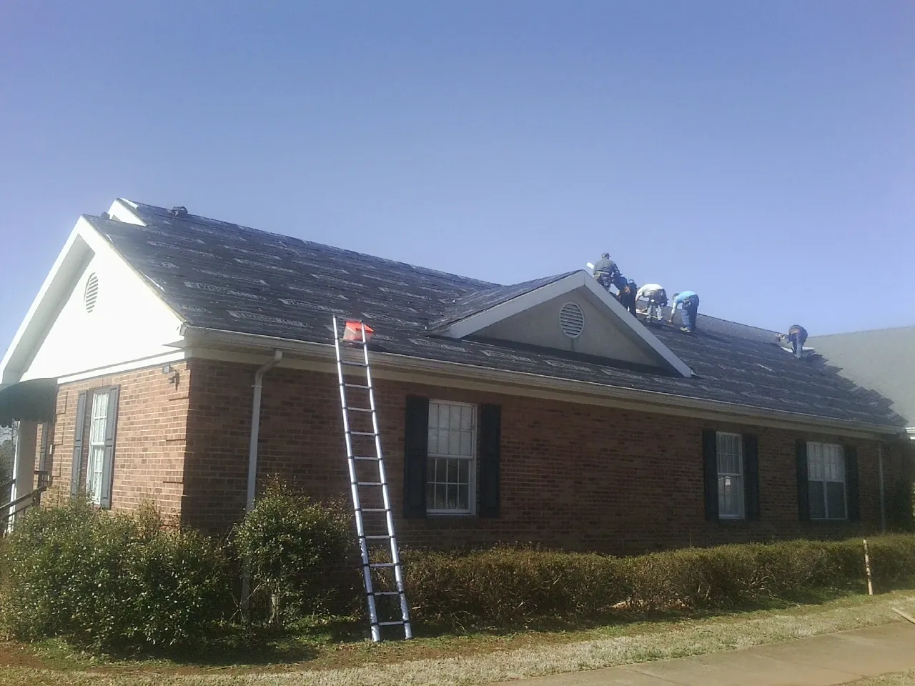 Crew tearing shingles off a brick ranch roof with a ladder set — Metal Roof Repair work by our crew in Ville Platte