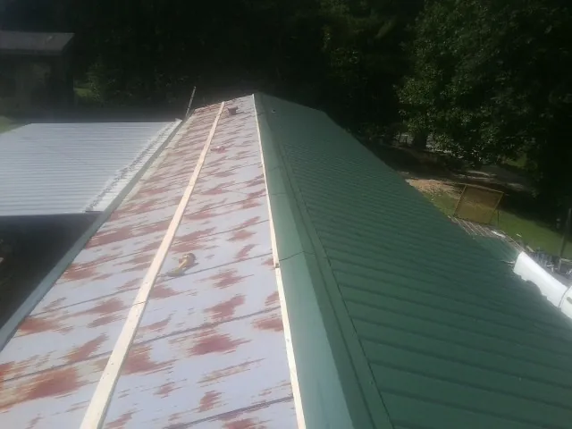 Old rusted panels beside newly installed green metal roofing — Wind Damage Roof Repair by Roofing Brothers in Ville Platte