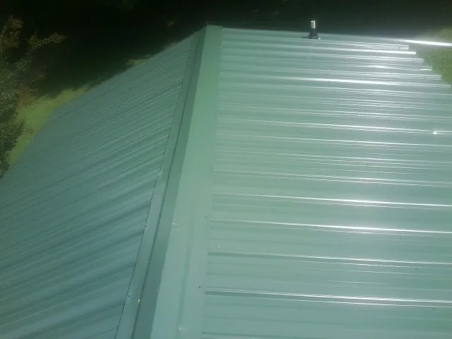 New green metal panels meeting at the ridge of a roof — Flat Roof Repair work by our crew in Ville Platte