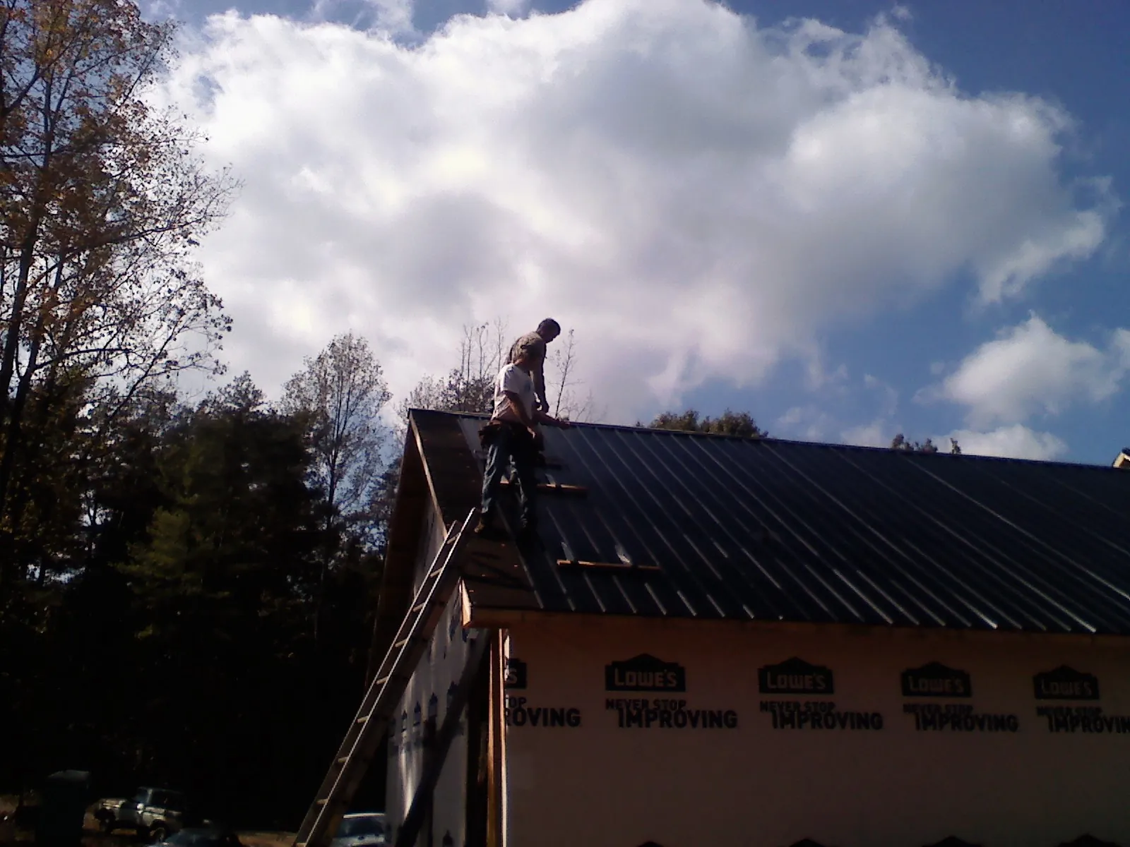 Roofer fastening dark metal panels high against a cloudy sky, from a Roof Inspection job in Ville Platte