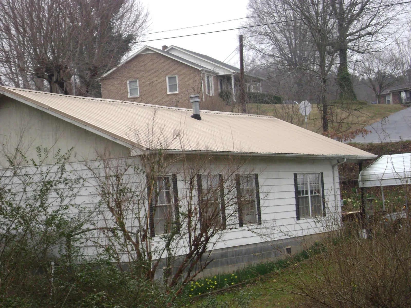 Tan metal roof on a white sided house set into a hillside — Commercial Roofing by Roofing Brothers in Ville Platte